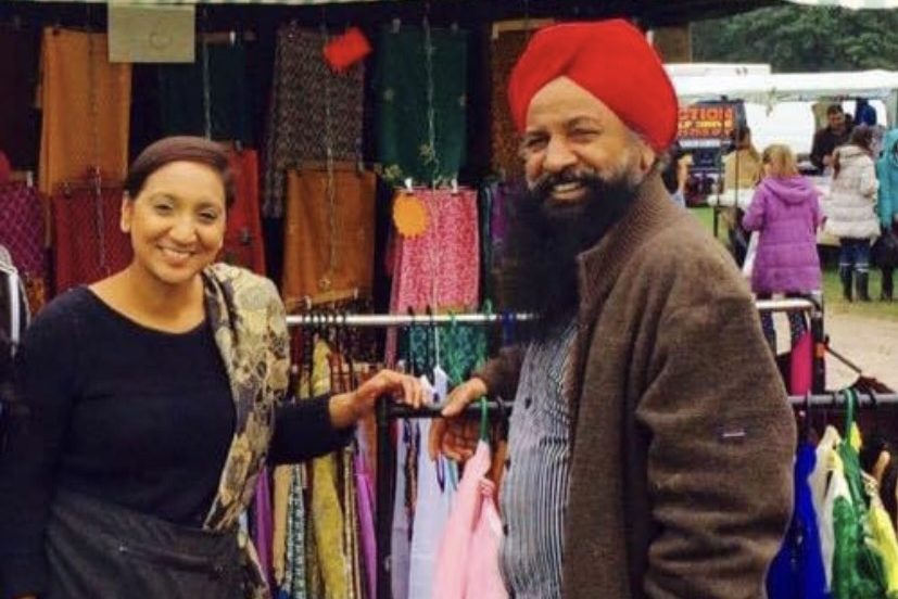 Satvir Kaur when she was younger, photographed with her dad at their market stall, with clothes and fabrics on racks for sale
